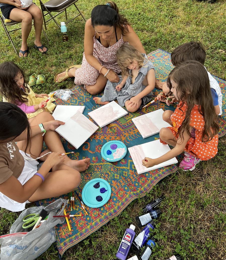 Crianças pintando telas ao ar livre, sentadas na grama com a Tia Thais